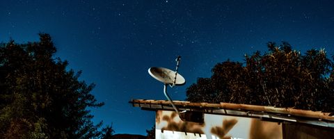 A satellite dish on a roof under a night sky